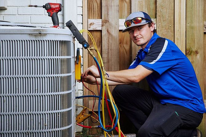 HVAC technician kneels to repair an AC unit, using tools outdoors.