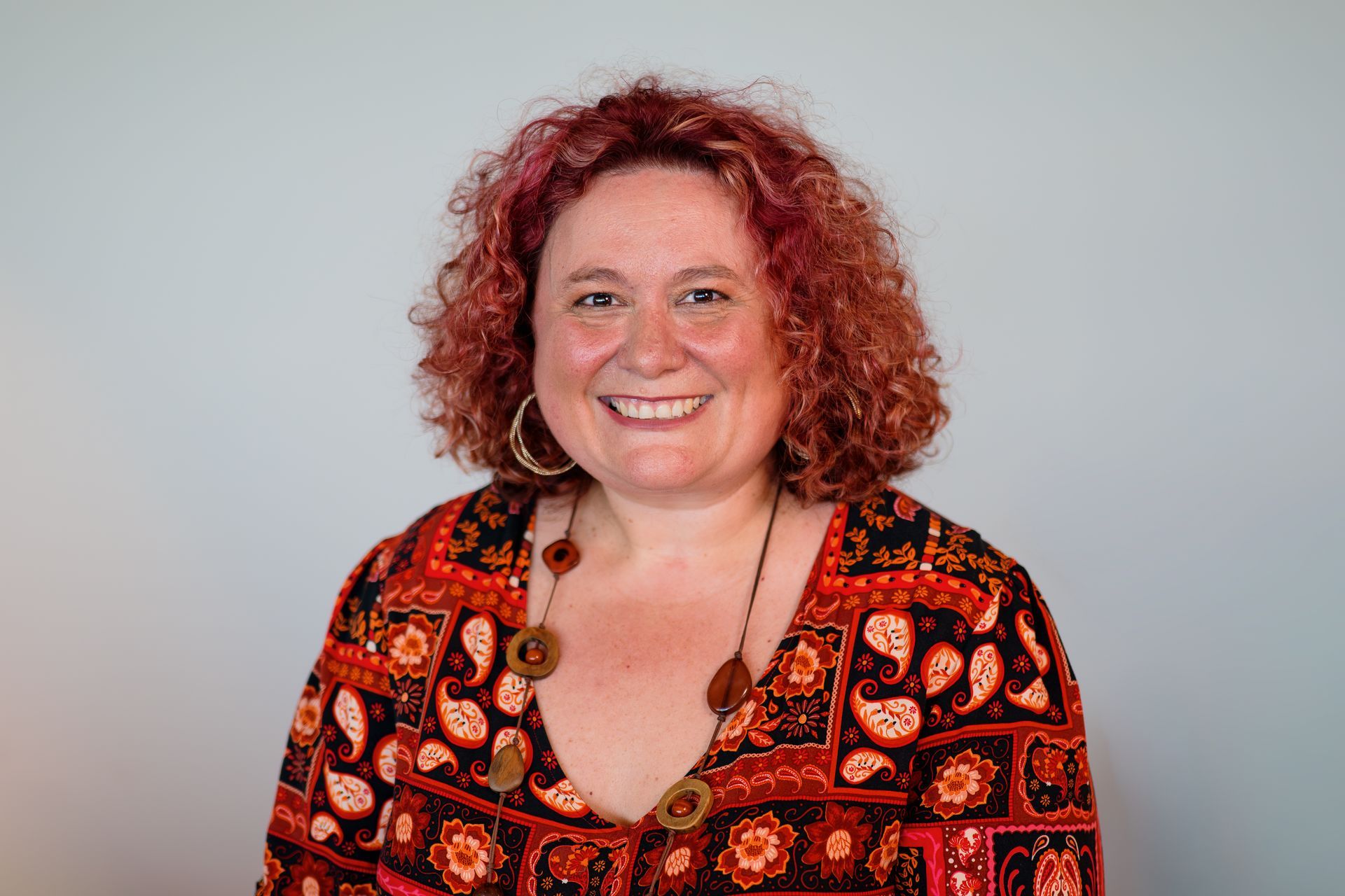 Aurora Bariatrics team member Claire Brown with curly hair wearing a patterned dress and dark cardigan, smiling in front of a geometric orange and cream background