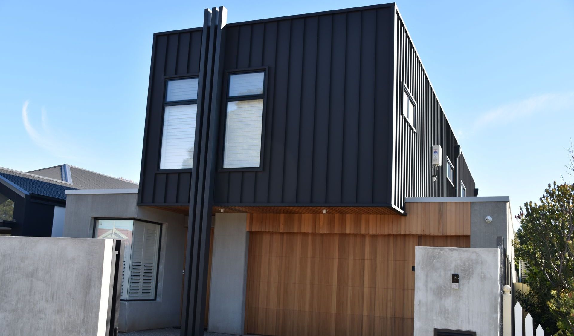 Modern two-story house with black exterior, wooden garage door, and light grey walls under a blue sky.