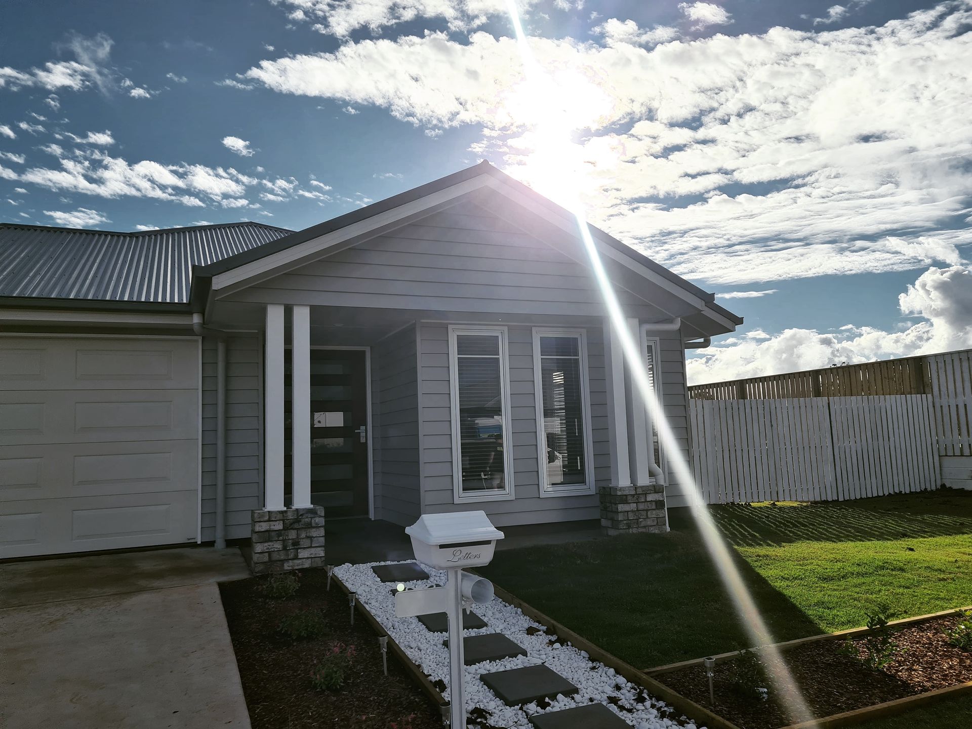 Gray house with a front porch and a white mailbox; bright sun shining.