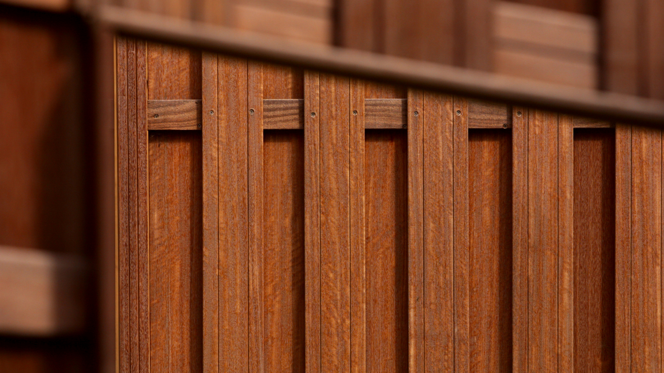 Wooden fence with vertical planks, secured by horizontal beams. The wood is a warm brown color.