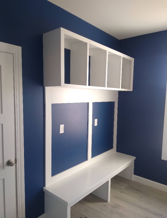 Built-in white desk and overhead shelves against a dark blue wall. The desk has two blue panels and a white frame.