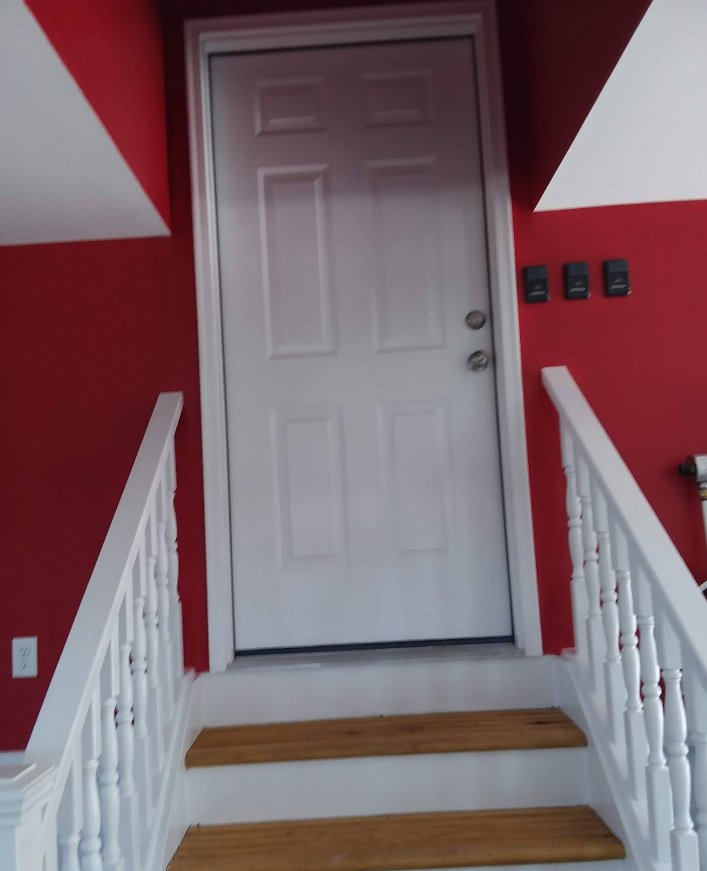 White door at the top of wooden stairs with white banisters, red walls, and three black switches on the right.