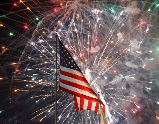 American flag waving before bright fireworks in the night sky