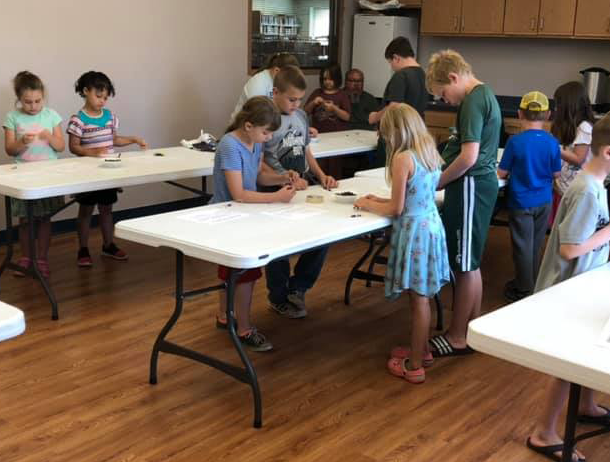 A group of children are standing around folding tables in a room.