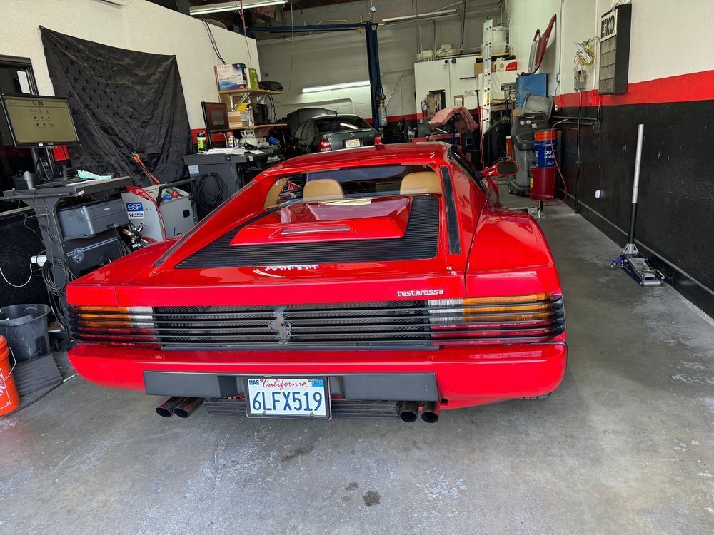 Red Ferrari Testarossa in a garage, California license plate, car being worked on.