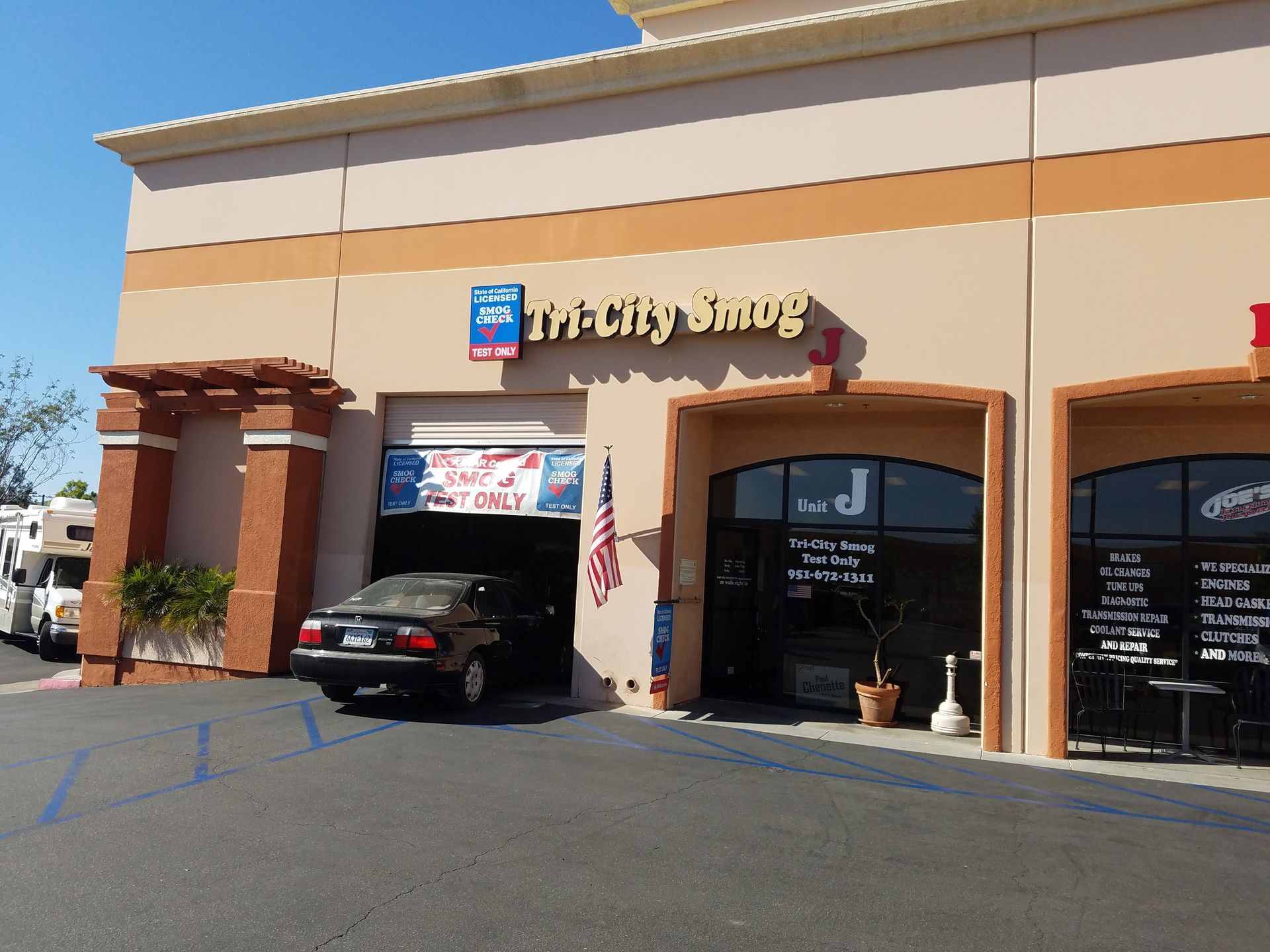 Exterior of The City Smog shop with a car inside the bay. Beige building with red brick accents.