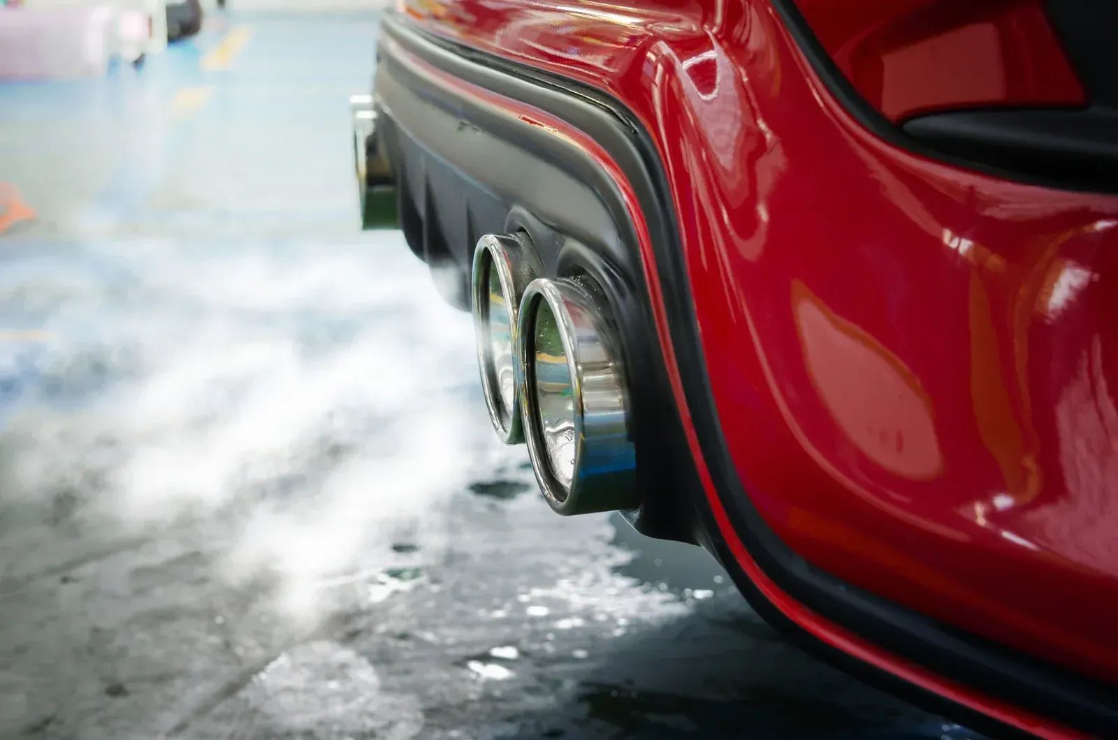 Red sports car with rear wheel spinning on icy pavement, spraying snow or smoke.