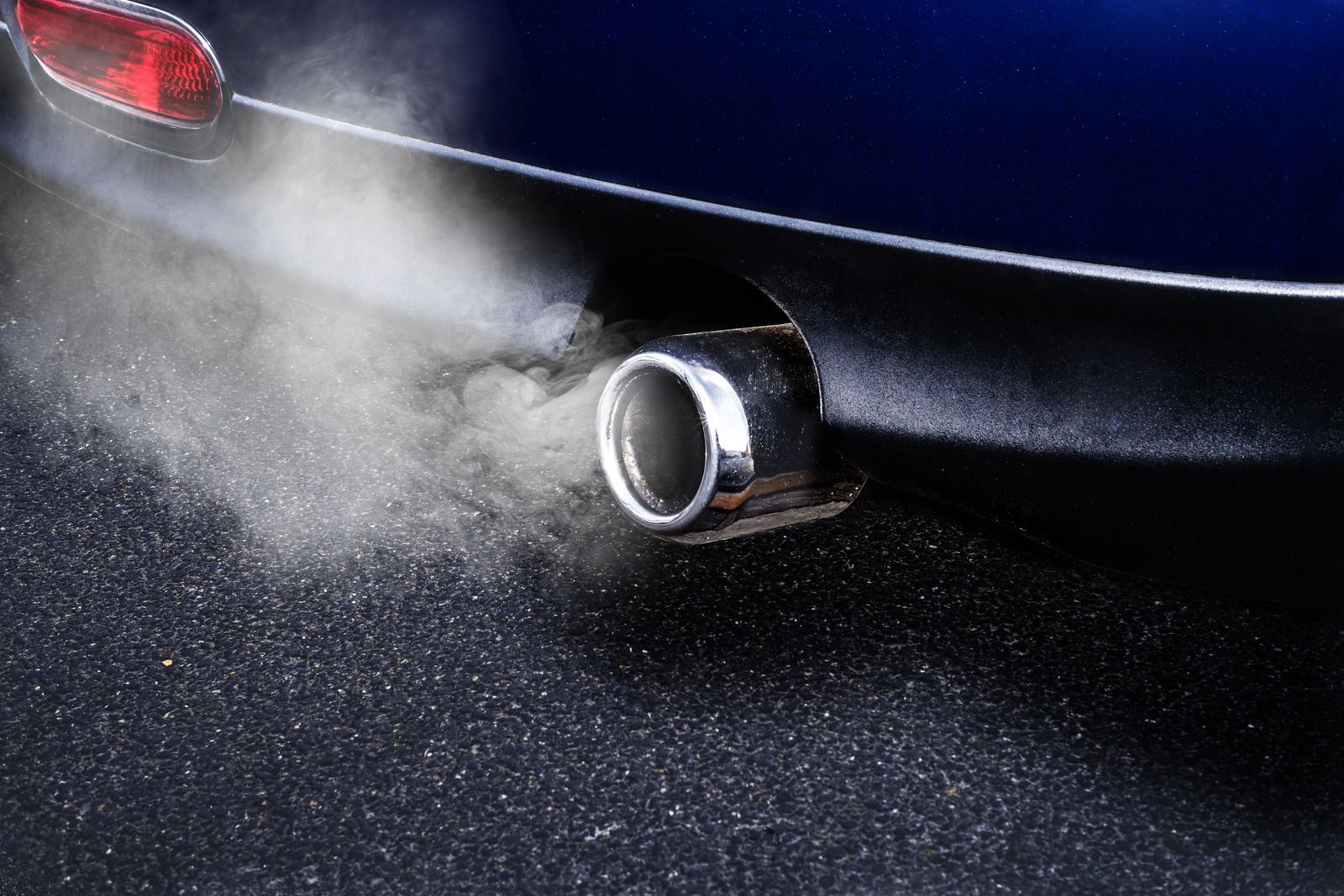 Car exhaust pipe releasing white smoke from a dark blue car on wet pavement