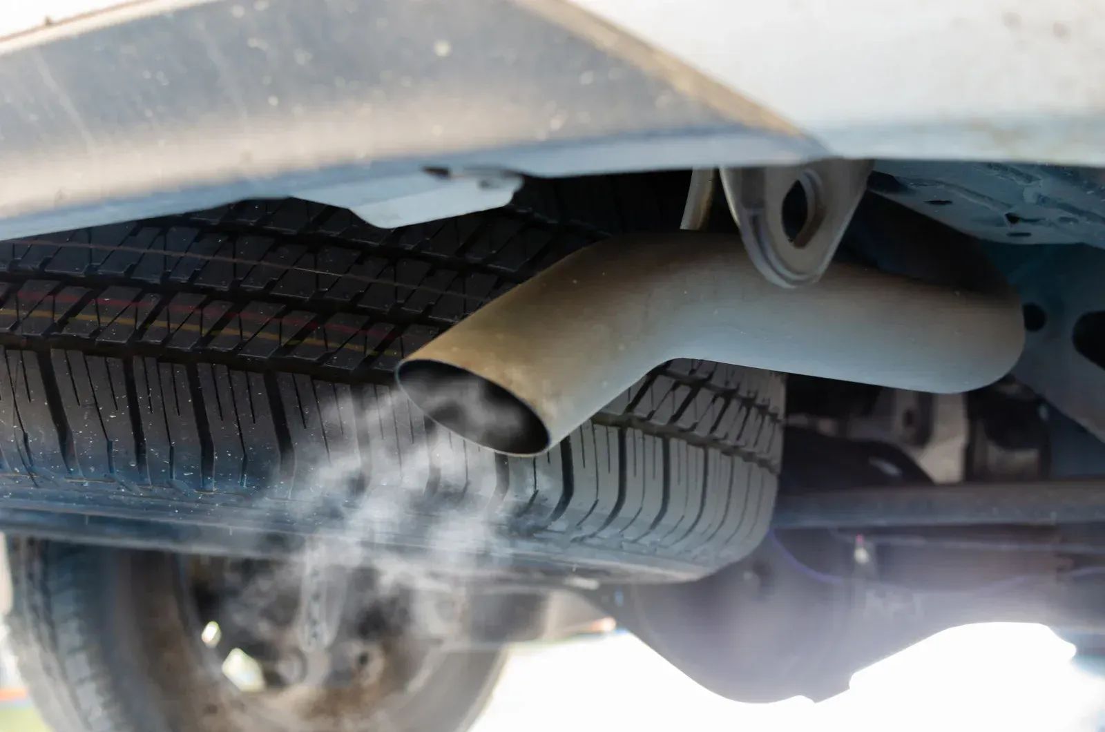 Underside of a car with white exhaust smoke billowing from the tailpipe near the rear tire