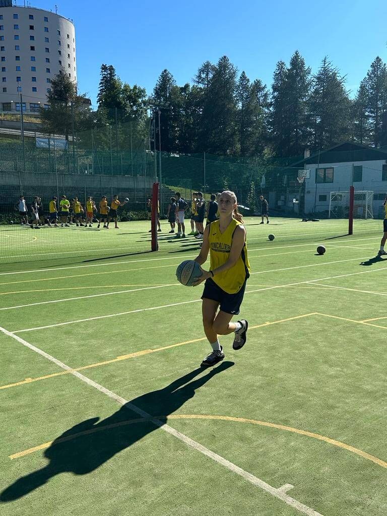 Una donna con una maglietta gialla corre con un pallone da basket su un campo.