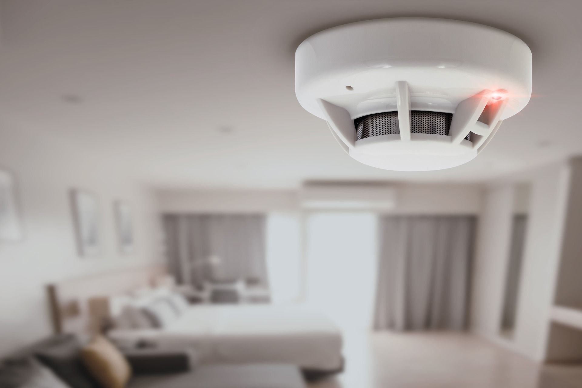 A smoke detector is mounted on the ceiling of a bedroom.