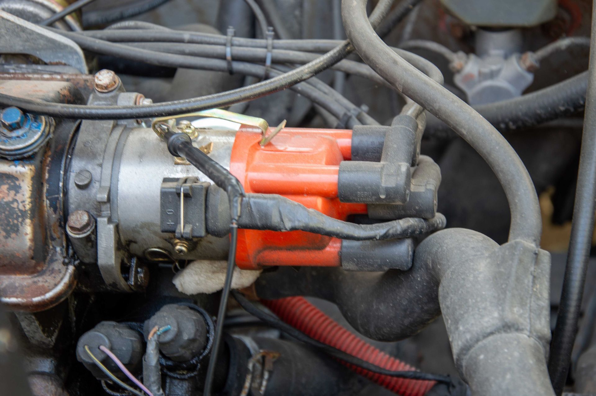 A bright orange ignition distributor cap attached to a car engine, surrounded by various black hoses and electrical wires.