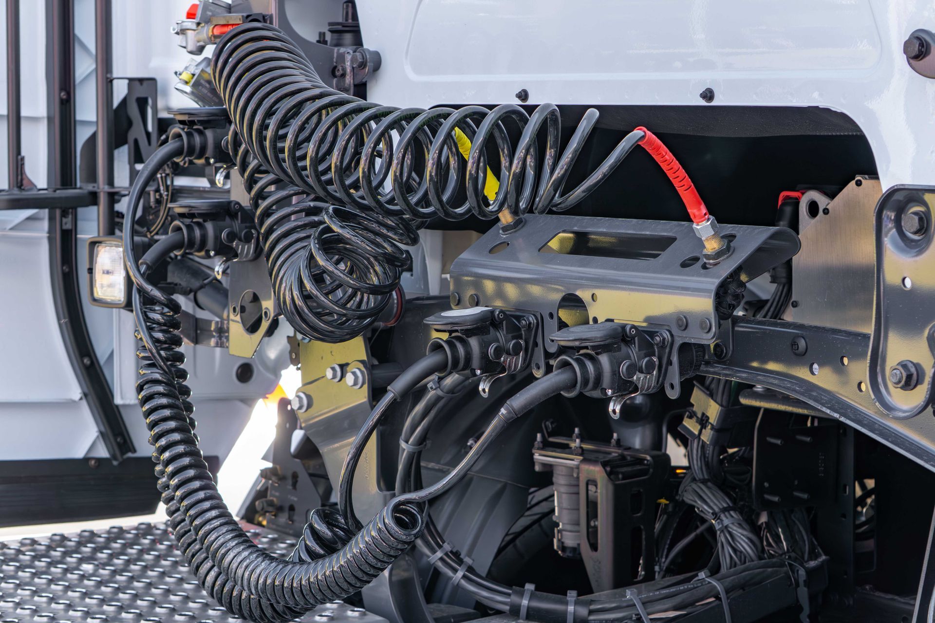 The back of a semi-truck cab with coiled black air hoses and electrical cables connected to a mounting bracket.