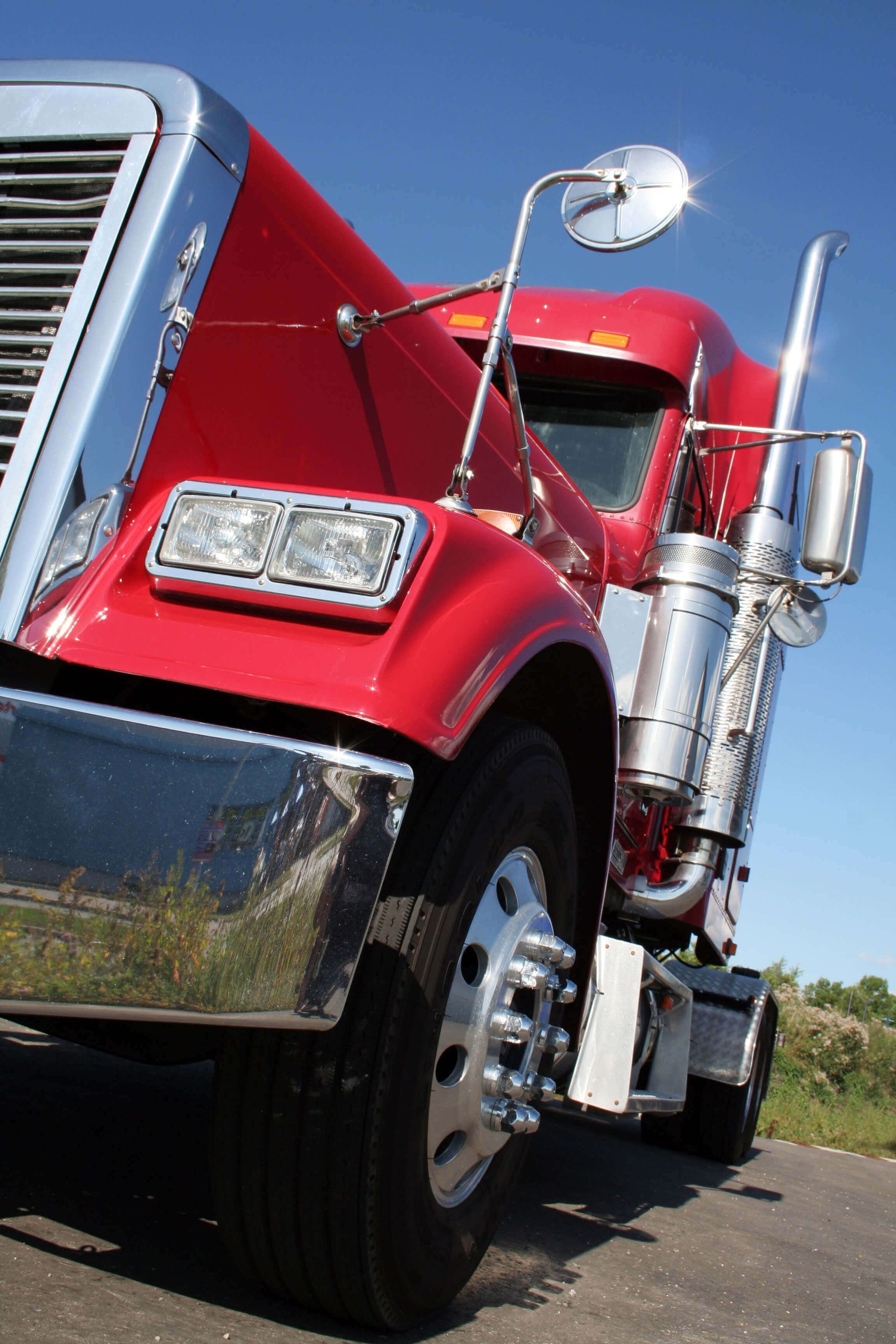 Camion semi-remorque rouge, détails chromés, stationné sur la route, ciel bleu en arrière-plan.