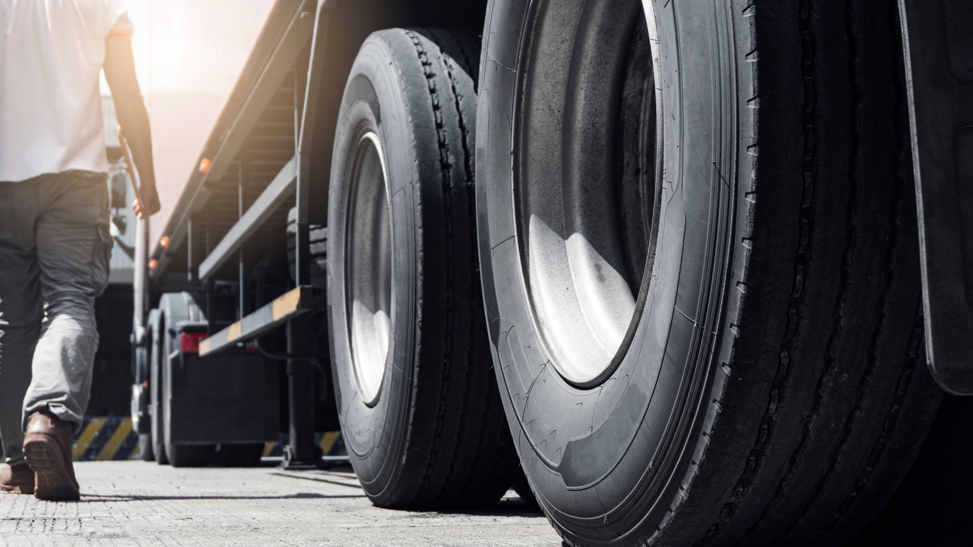 Une personne passe à pied devant les roues arrière d'un semi-remorque sur l'asphalte.