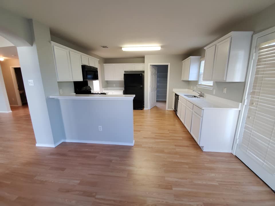 An empty kitchen with white cabinets and hardwood floors.