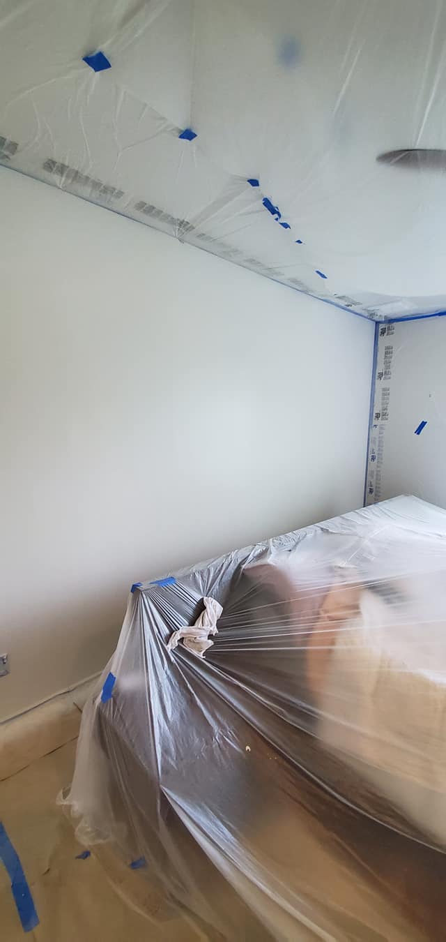 A bedroom is being painted and covered in plastic.