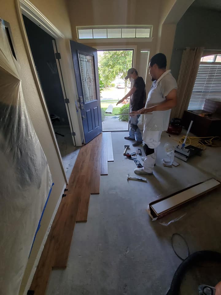 Two men are installing hardwood flooring in a hallway.