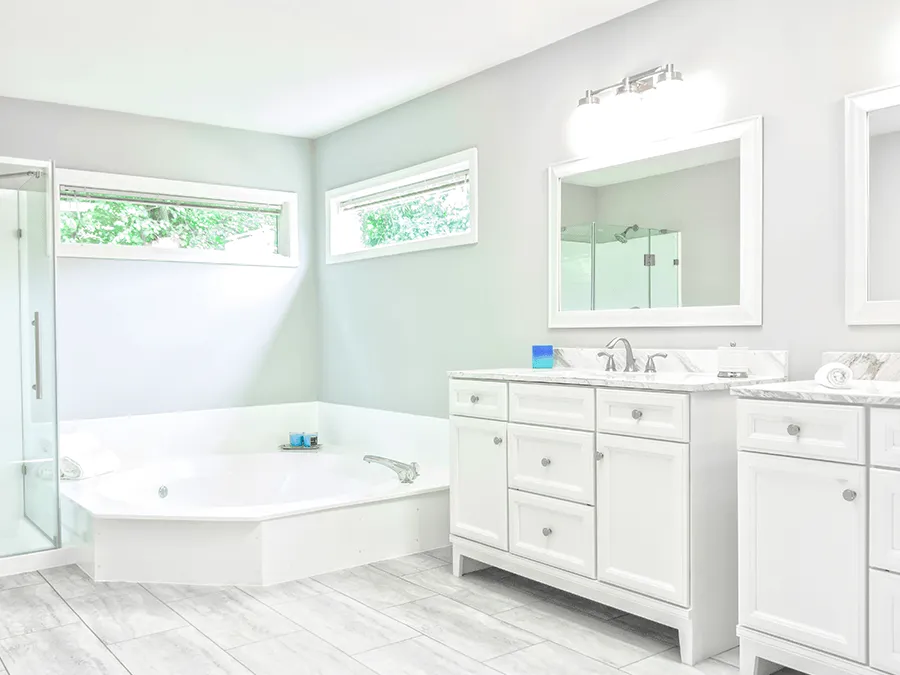 A bathroom with white cabinets , sinks , mirrors and a tub.