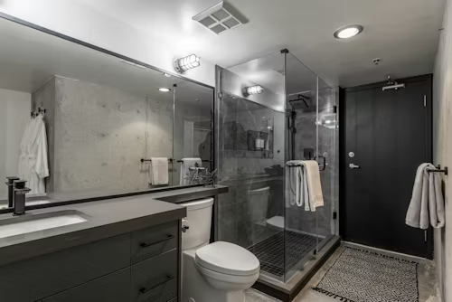 Modern bathroom with gray vanity, shower, and black door.