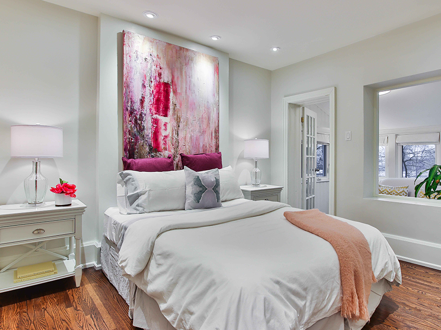 A bedroom with a large painting on the wall above the bed.