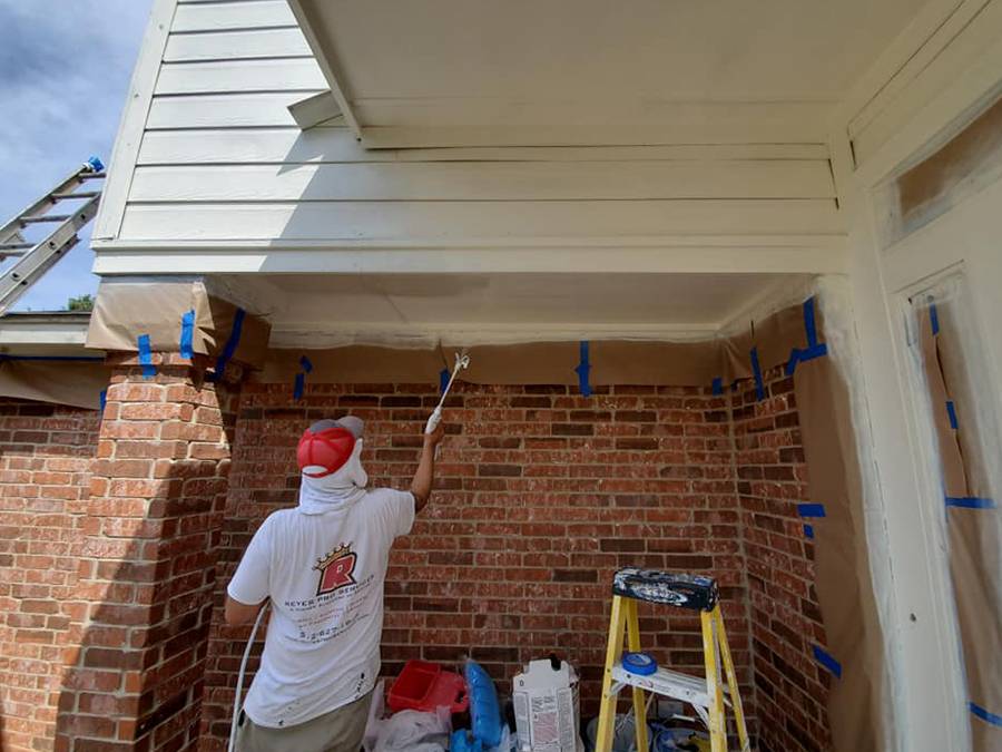 A man is painting the ceiling of a brick house.