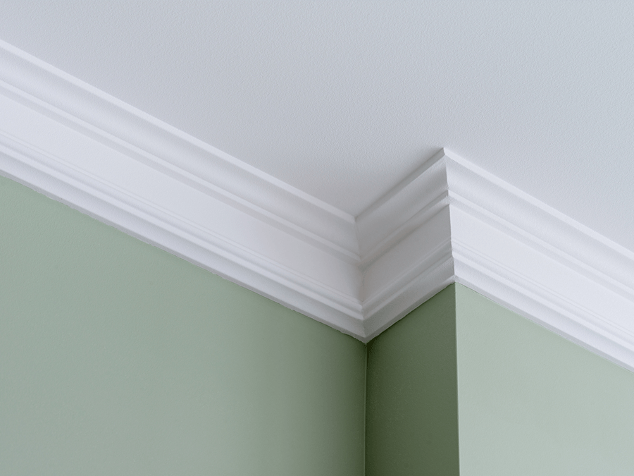 A corner of a room with green walls and white molding on the ceiling.