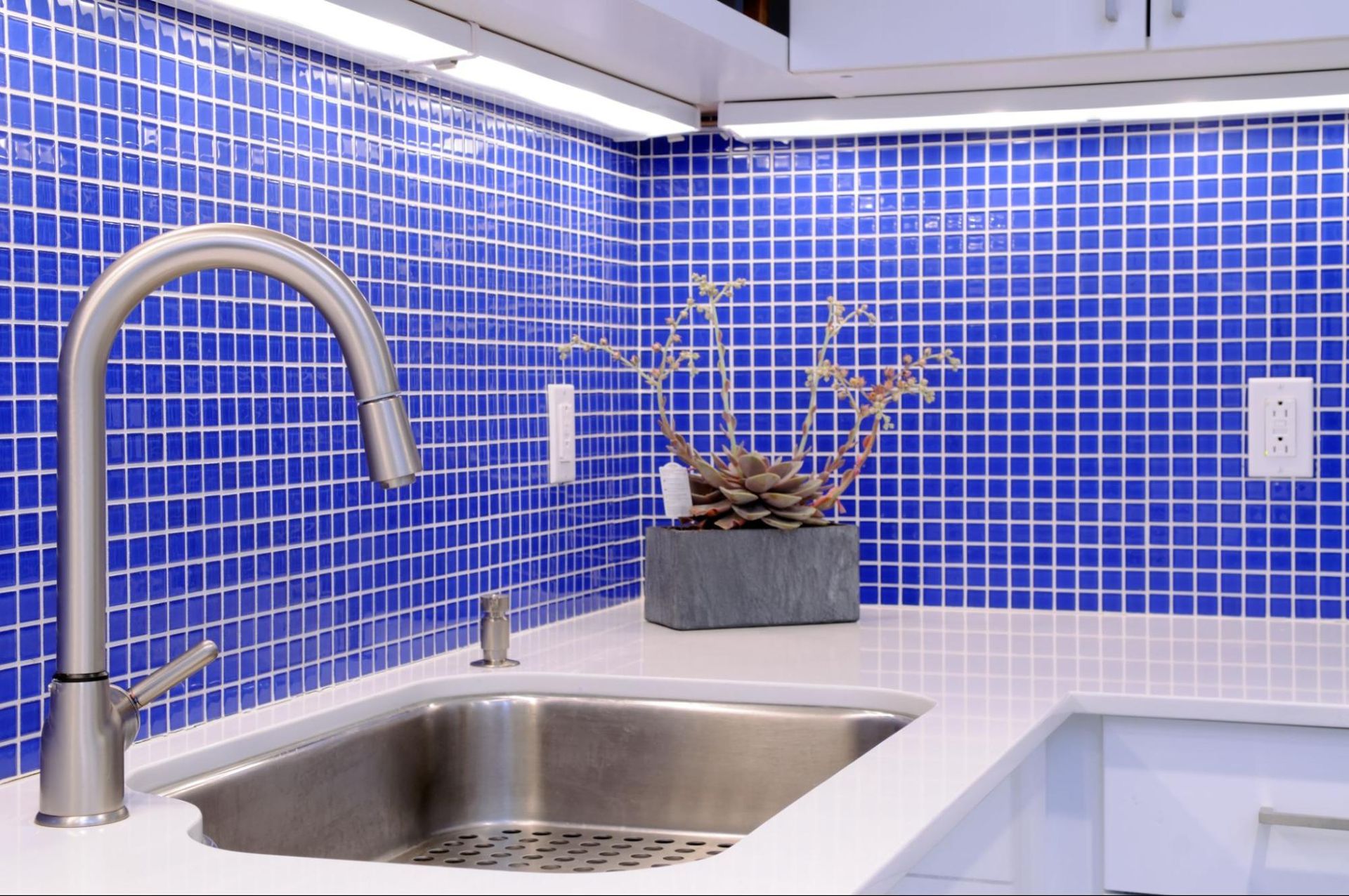 A kitchen with blue tiles and a stainless steel sink