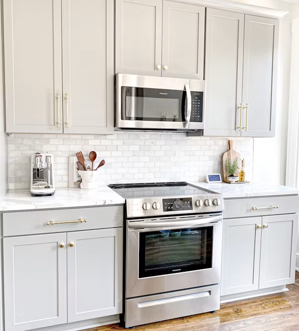 Bright white kitchen with stainless steel stove and microwave, white cabinets, and wood floor