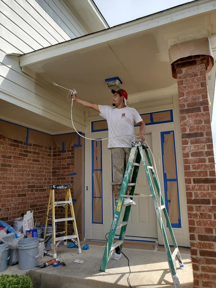 A man is standing on a ladder painting a house.
