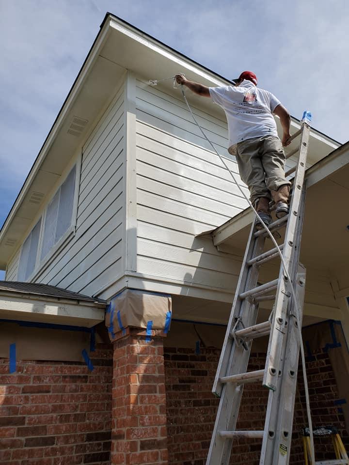A man on a ladder is painting the side of a house.