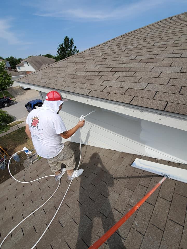 A man is painting the side of a house with a sprayer.