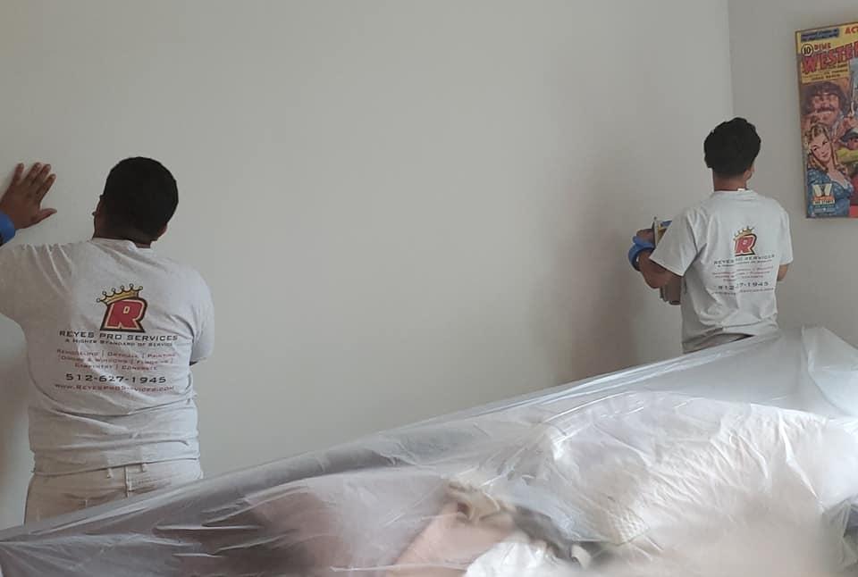 Two men are painting a wall in a room.