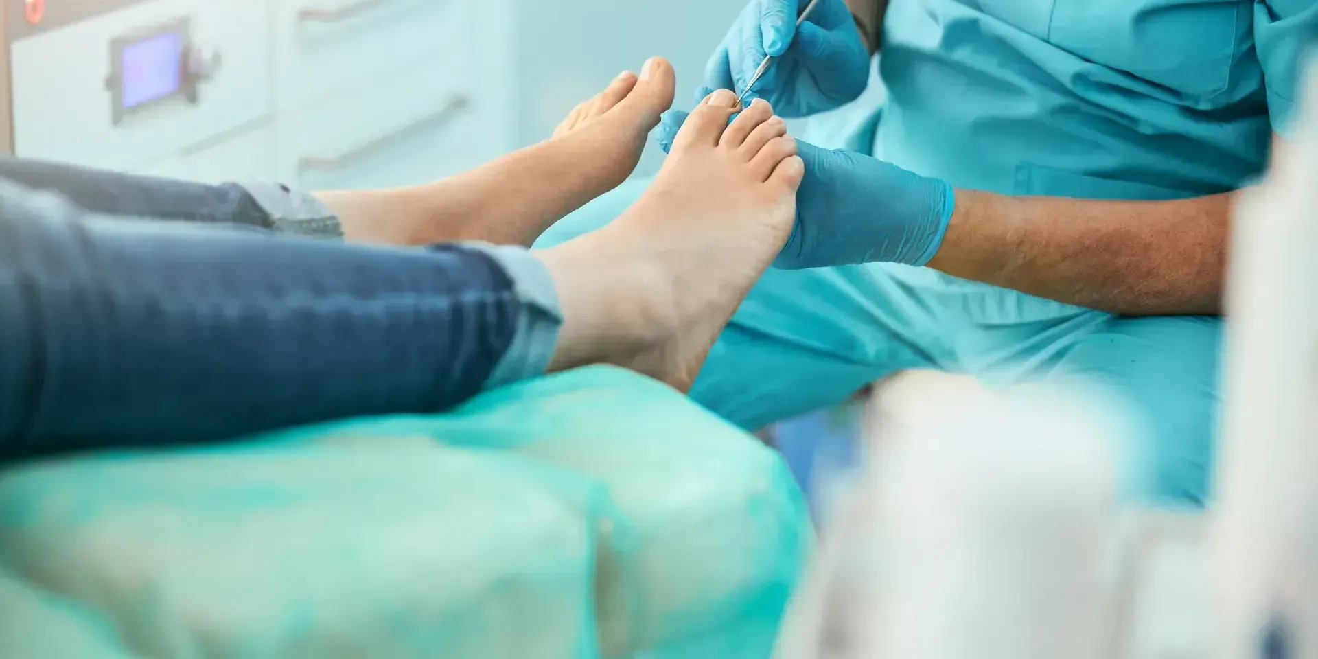 A healthcare professional wearing teal scrubs and gloves performs a foot examination on a patient.