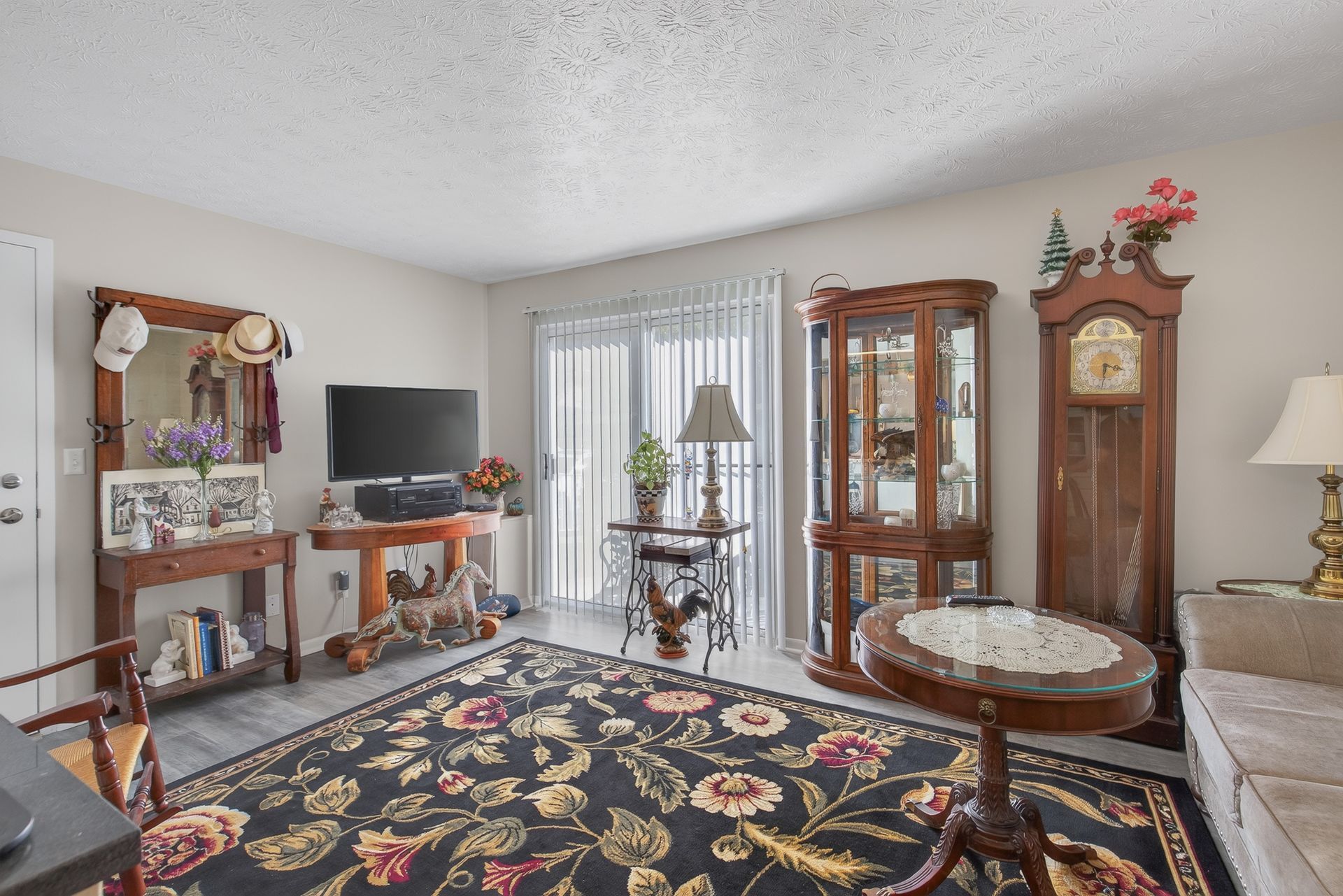 Elegant living room with floral rug, grandfather clock, glass cabinet, and TV on a wooden console.