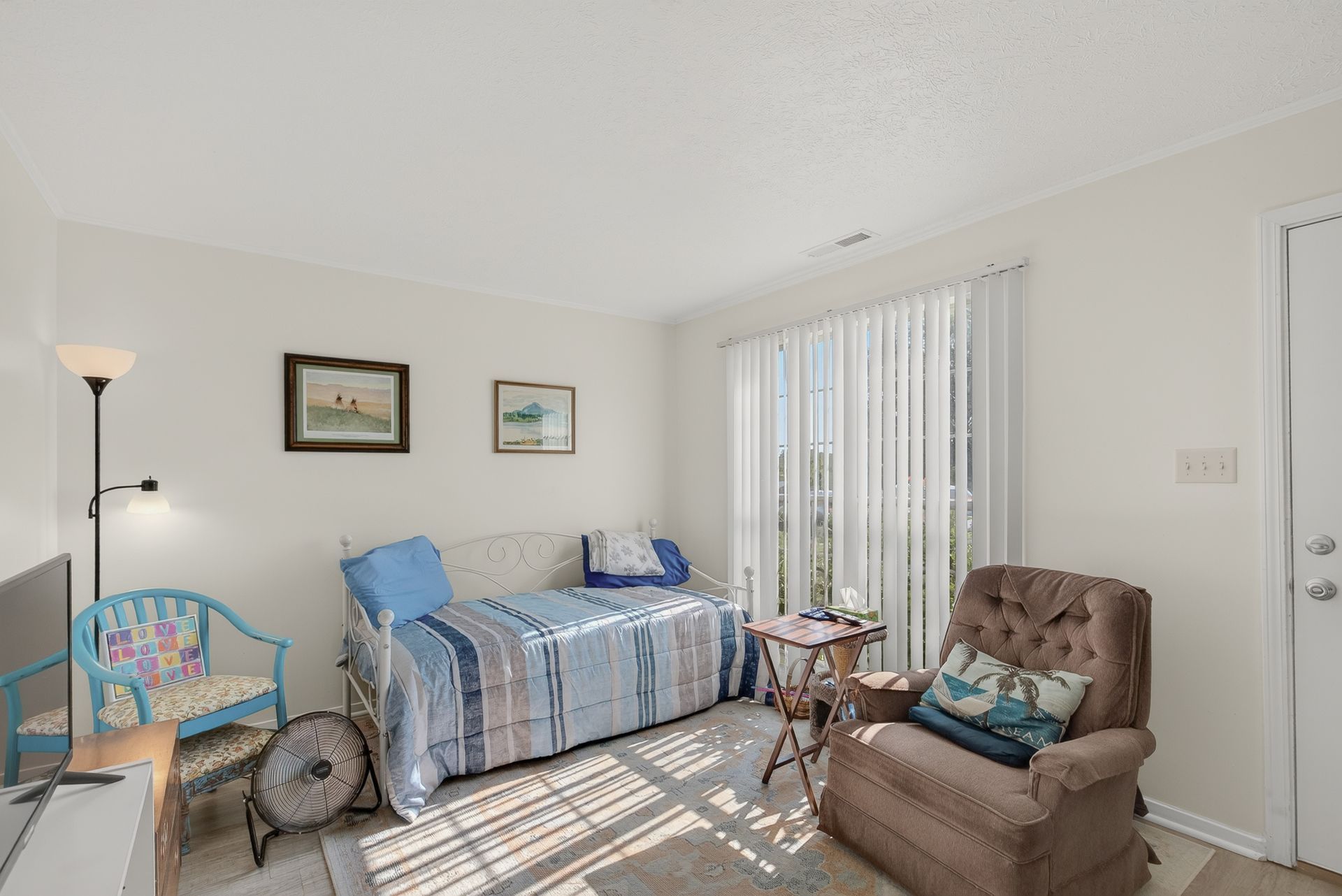 Bright living room with blue-striped sofa, brown recliner, floor lamp, and vertical blinds