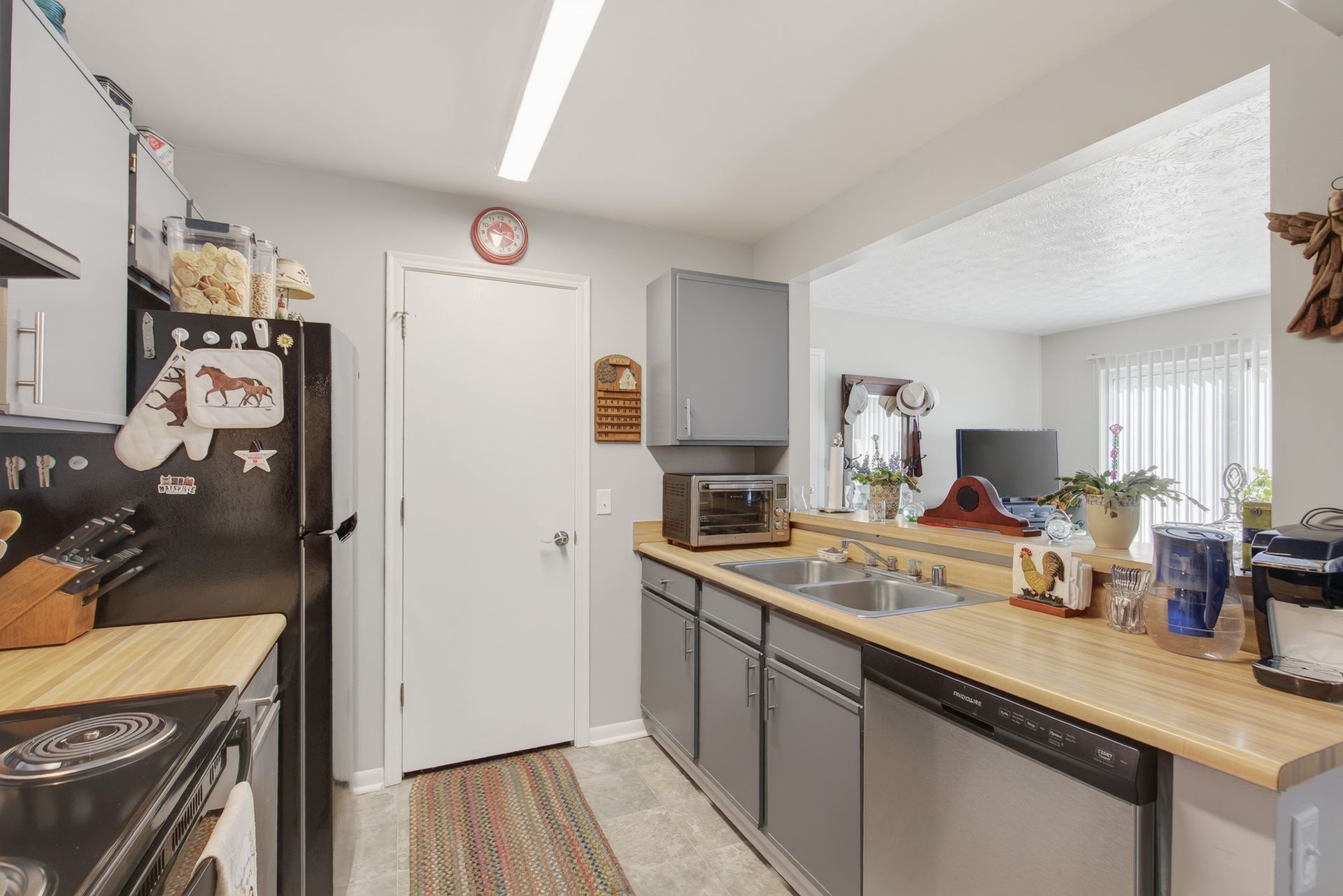 Bright kitchen with gray cabinets, wood countertops, and a white door at the end.
