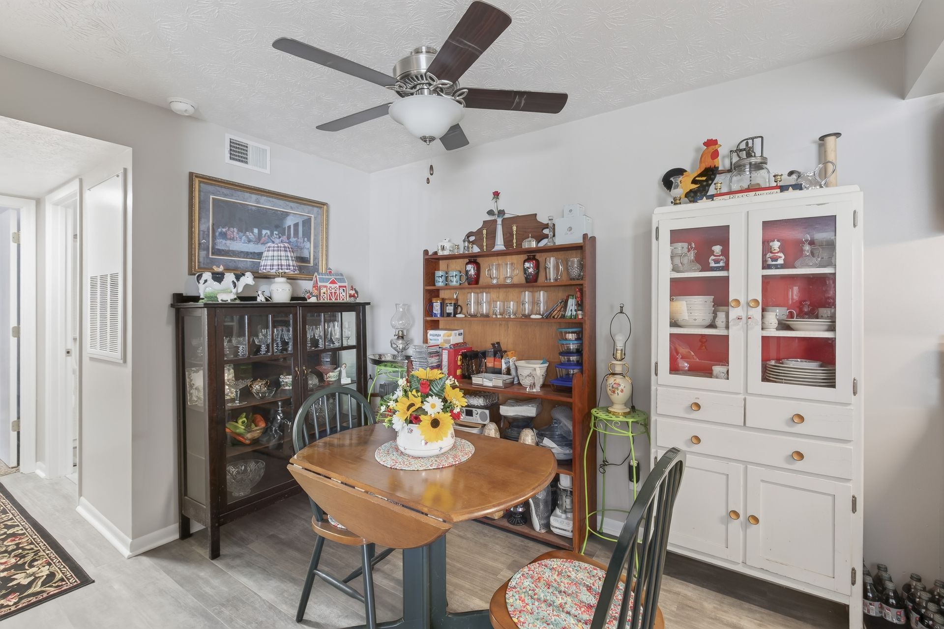 Bright dining room with round wooden table, hutch cabinets, and ceiling fan in a white interior.