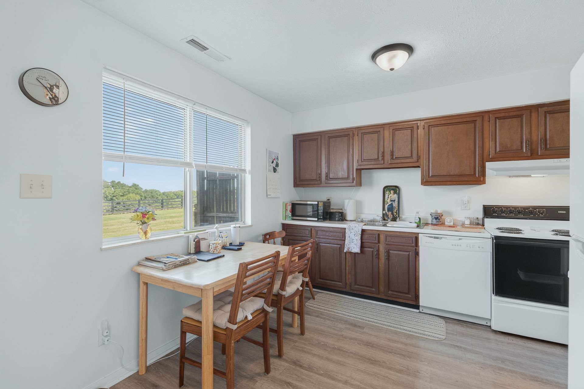 Bright kitchen with wooden cabinets, white appliances, and a small table by a large window.