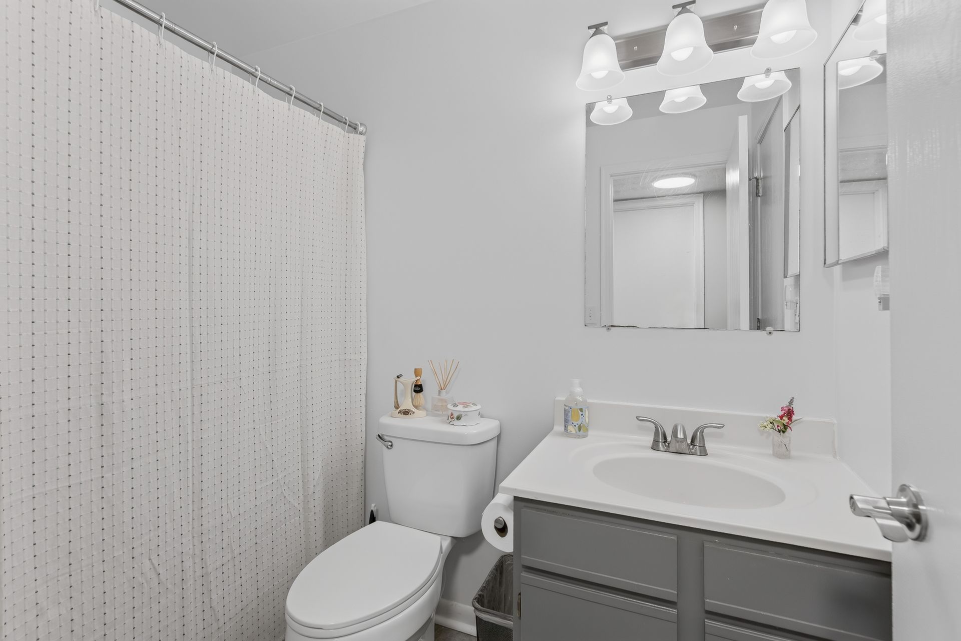Small white bathroom with toilet, vanity sink, mirror, and shower curtain.