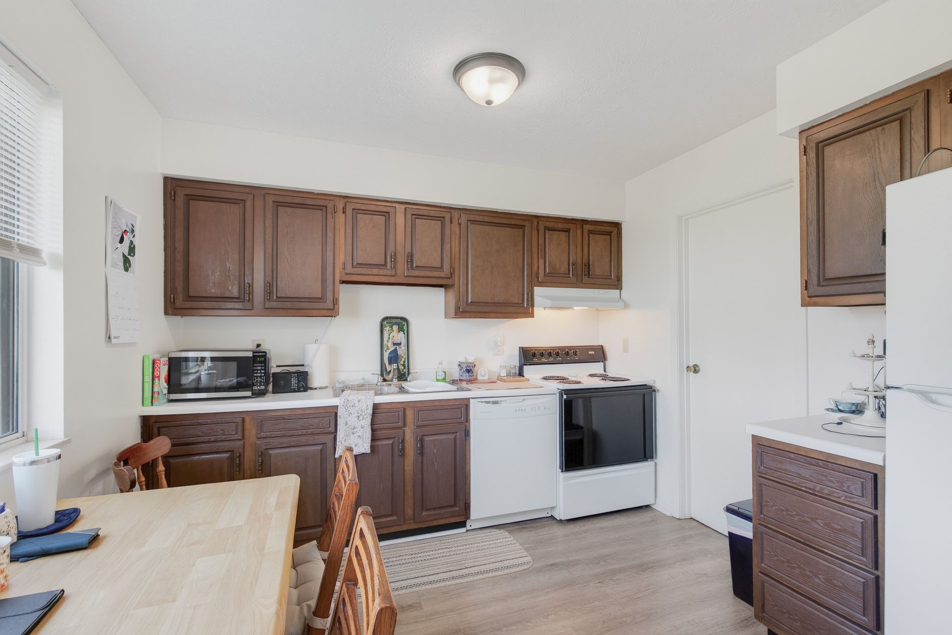 Small kitchen with wood cabinets, white appliances, and a dining table by the window