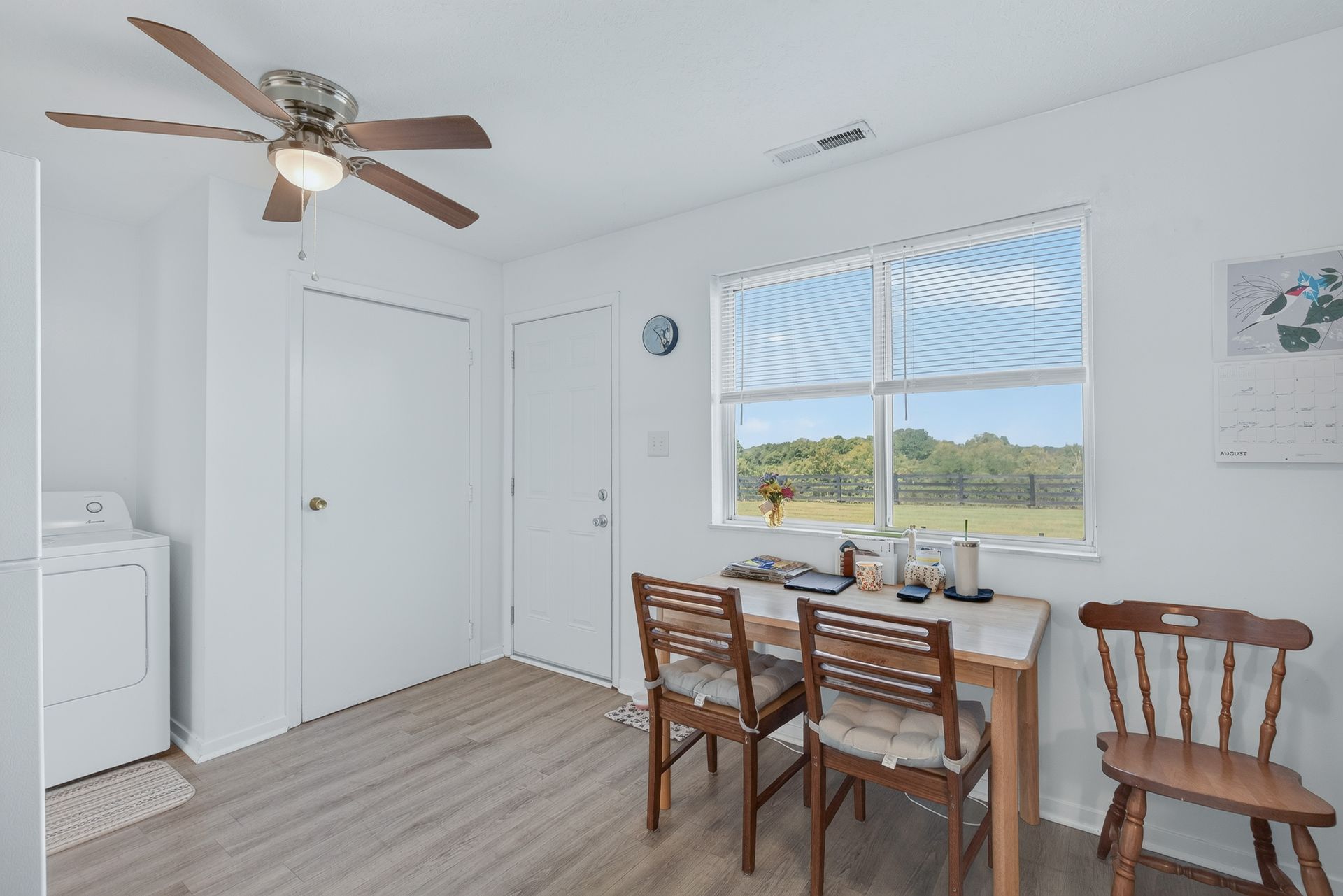 Small dining area with wooden table and chairs, ceiling fan, and window overlooking a bright yard.