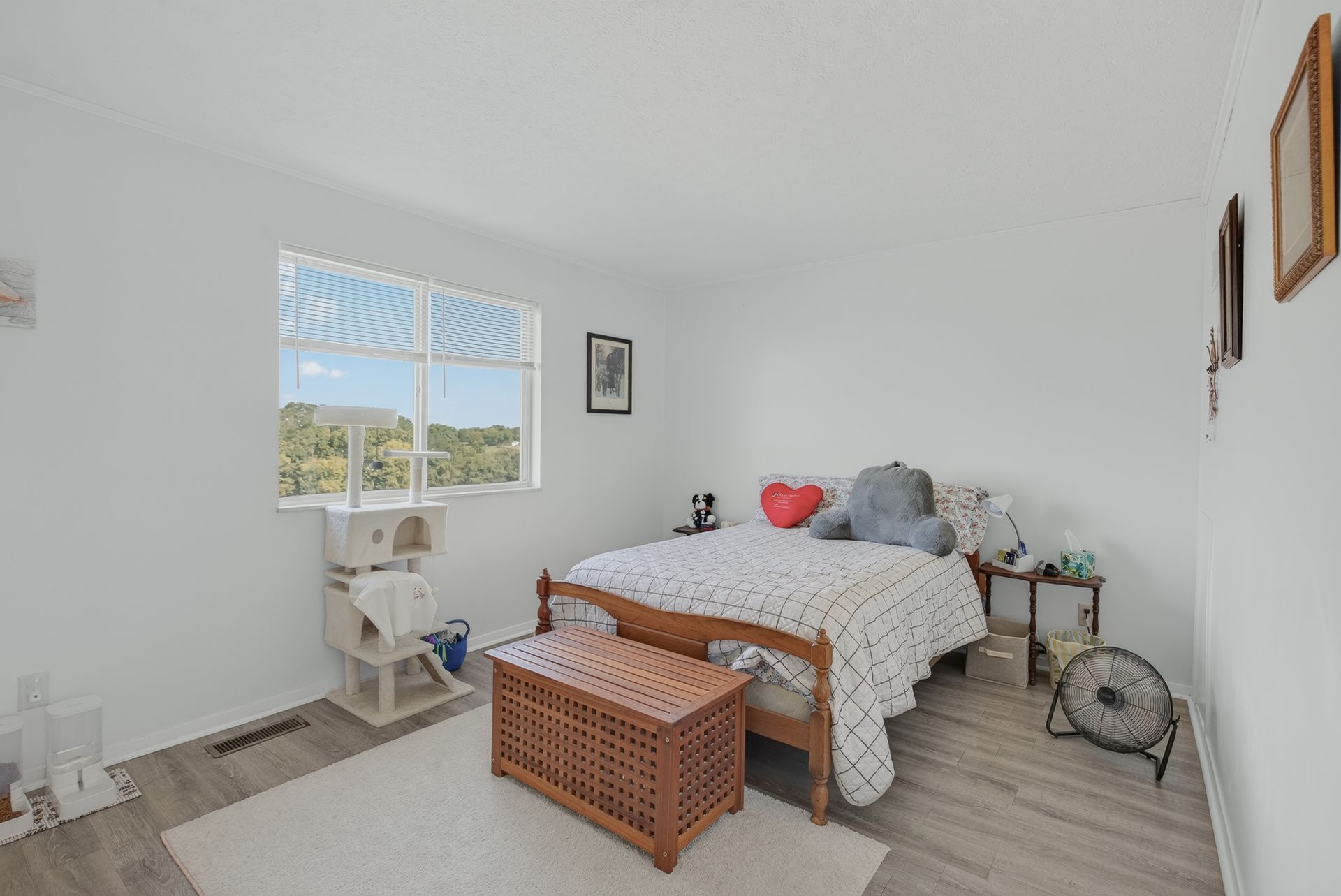 Bright bedroom with a bed, wicker bench, white walls, and a window overlooking greenery.
