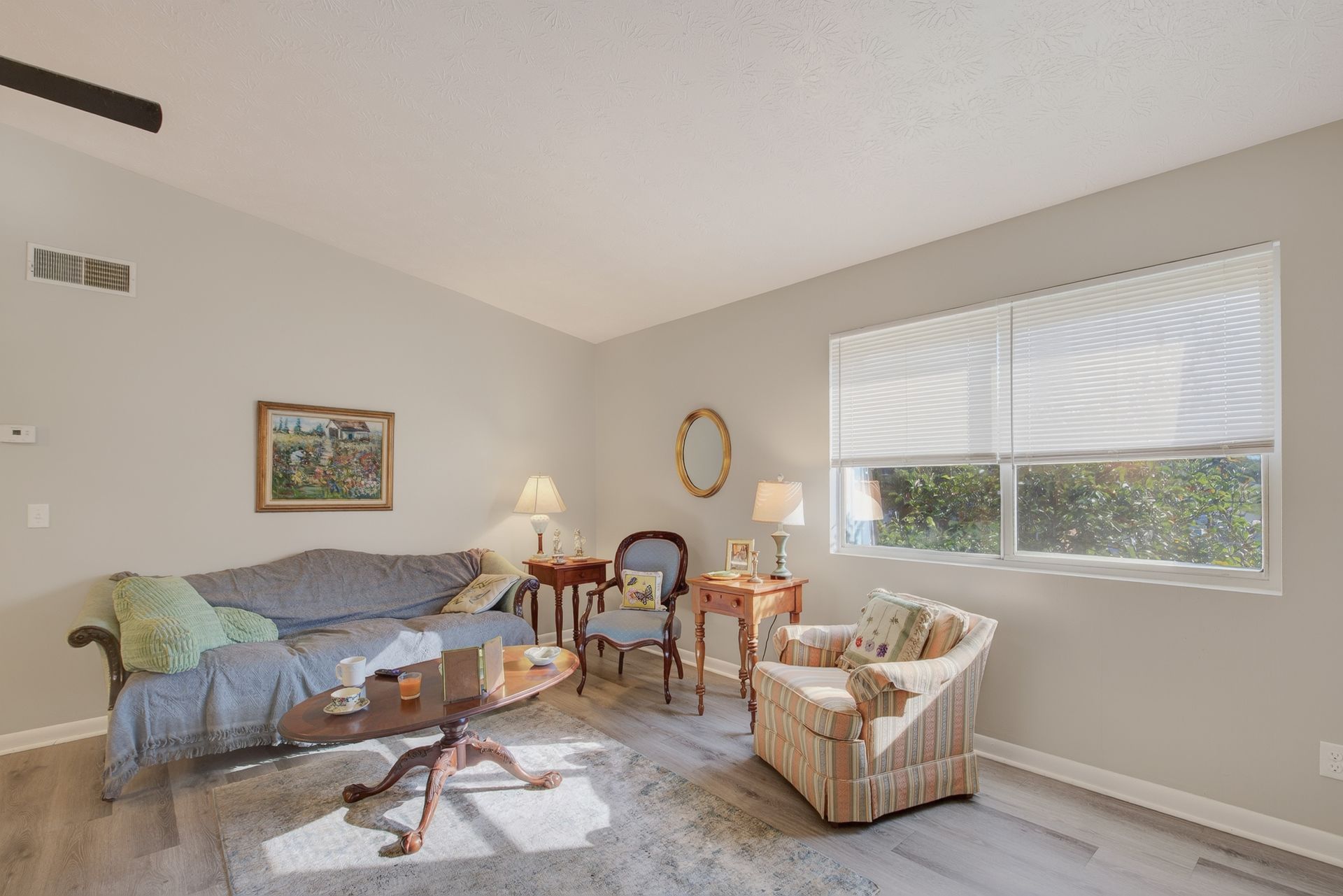 Bright living room with sofa, wicker chairs, coffee table, and large window with blinds