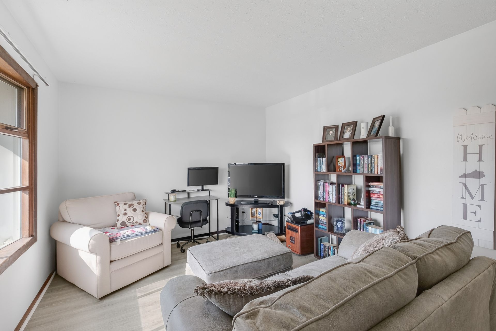 Bright living room with beige sofas, TV, bookshelf, and a window on the left.