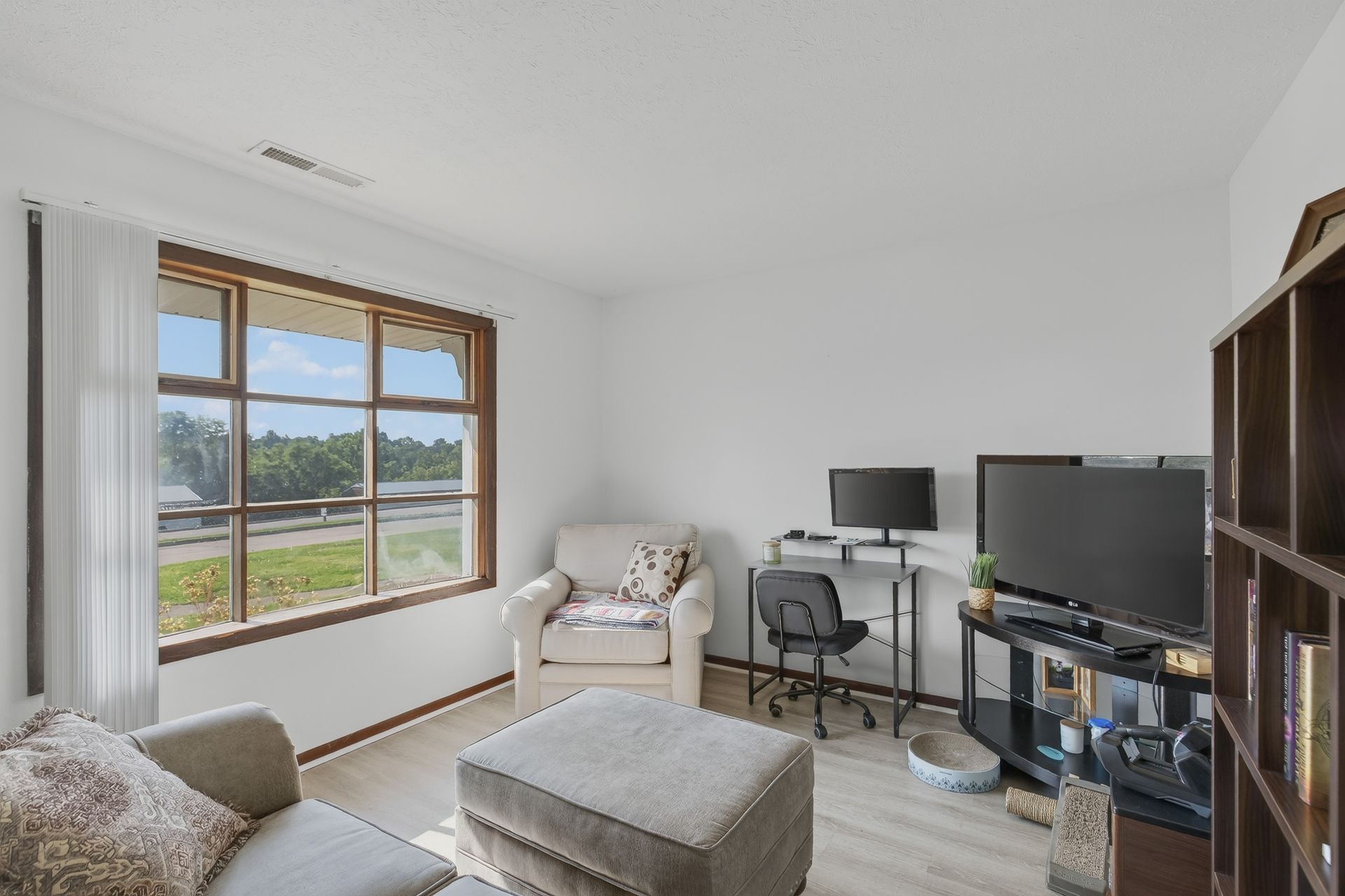 Bright living room with large window, beige chair and ottoman, TV stand, and wooden cabinet.