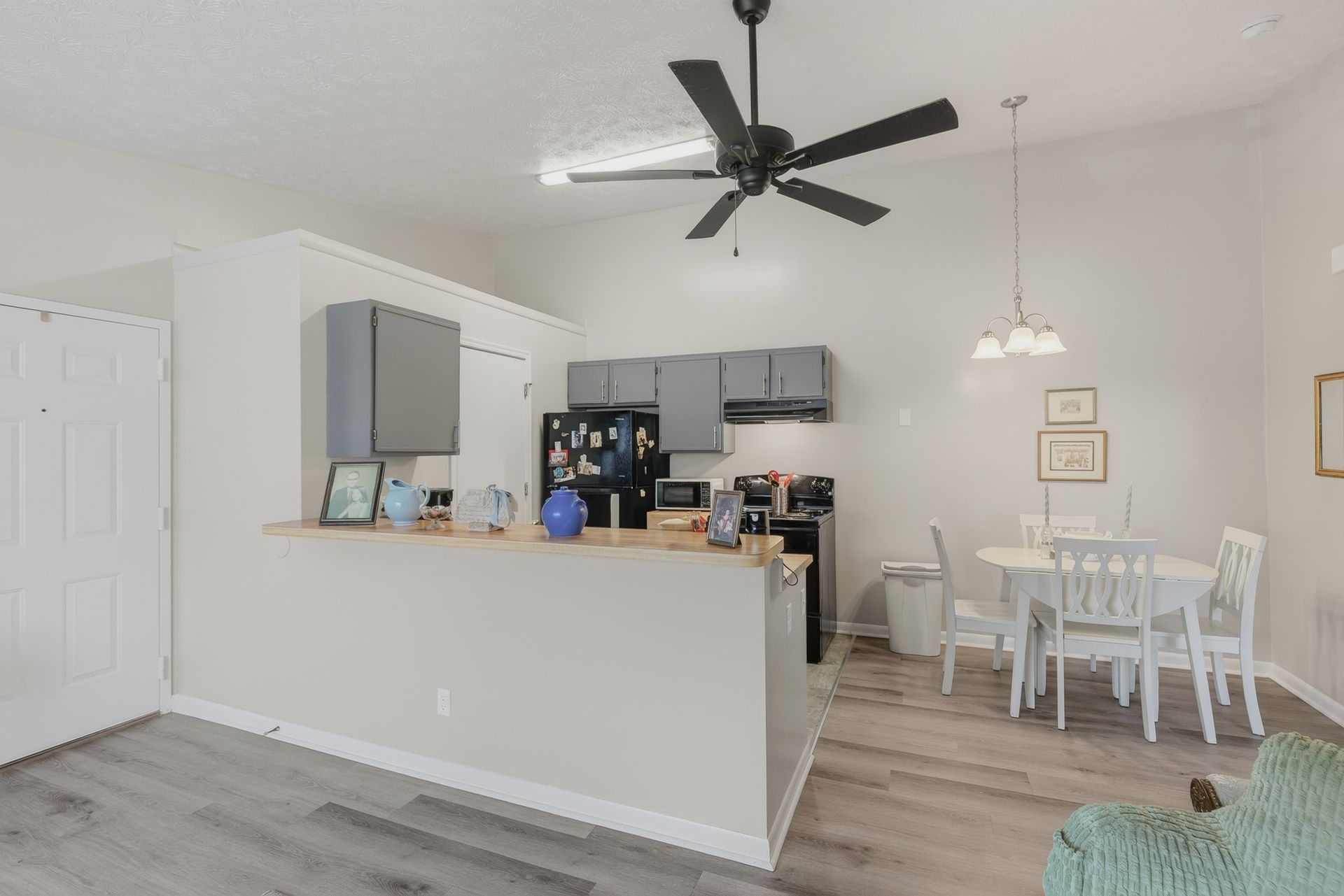 Open kitchen and dining area with white cabinets, gray counters, and a ceiling fan above hardwood floors