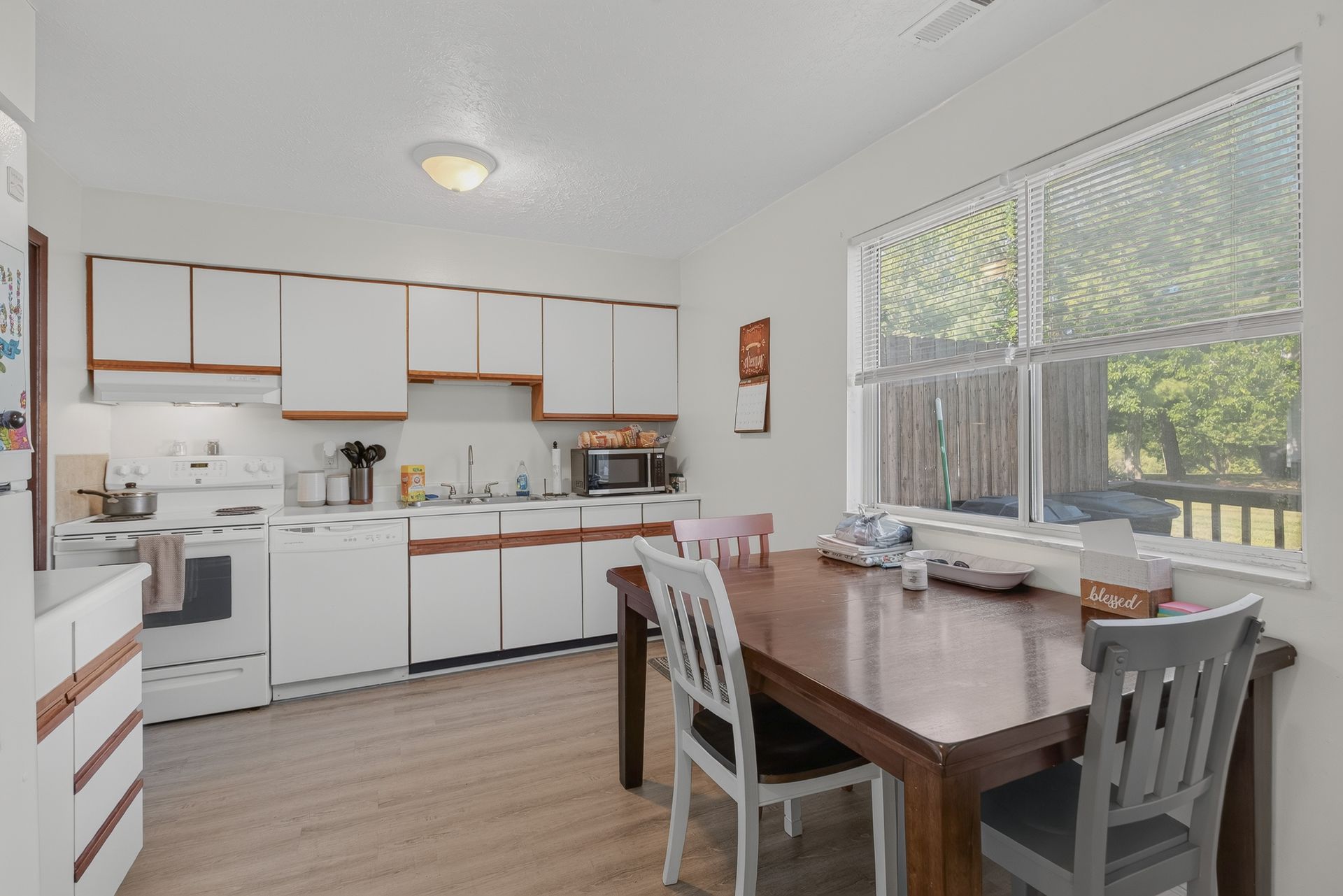 Bright kitchen with white cabinets, wooden table, and large windows letting in natural light