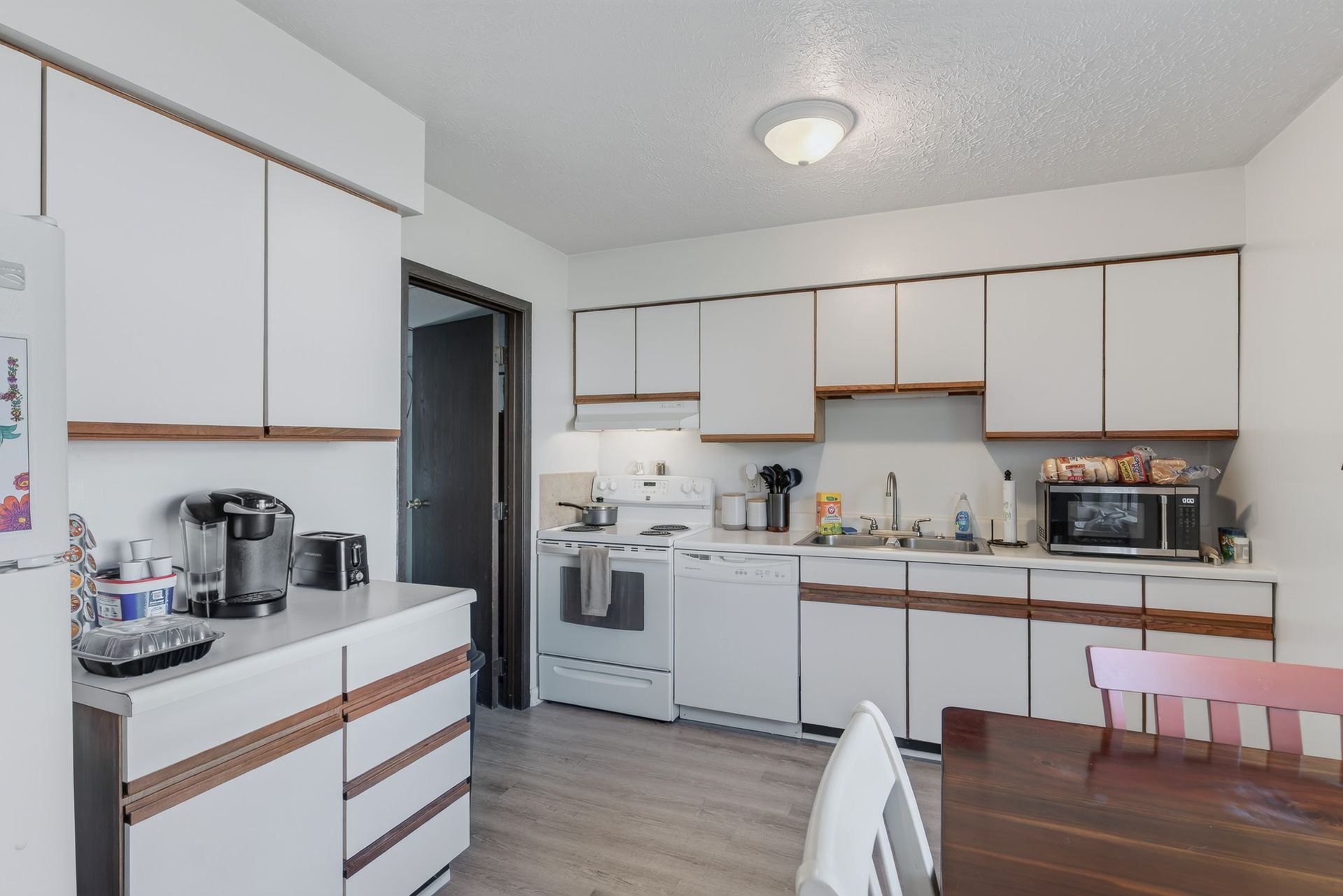 Bright white kitchen with cabinets, stove, sink, and dining table by a windowless wall